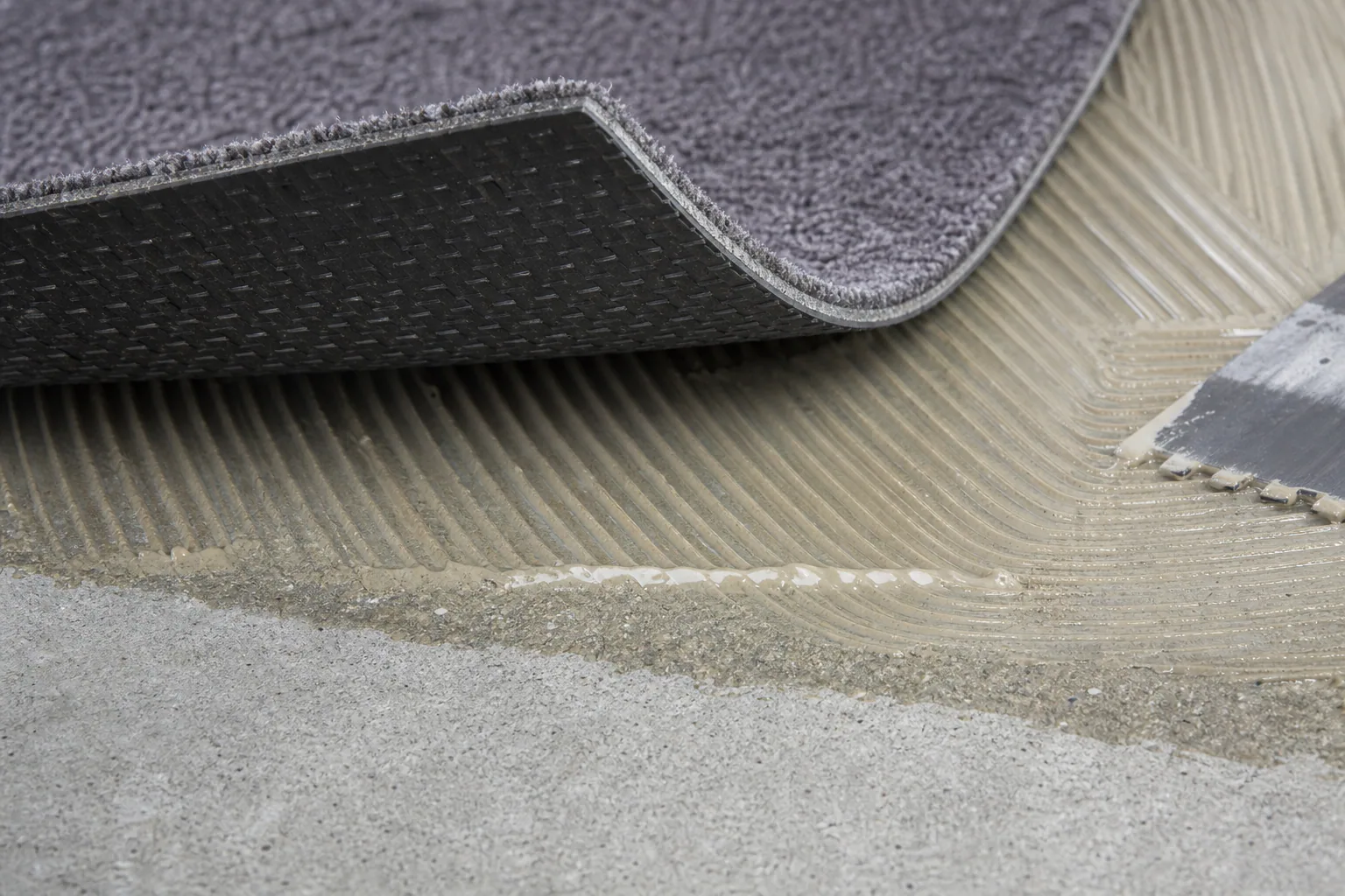 Close-up of commercial carpet tile backing, adhesive and concrete substrate during a compatibility review