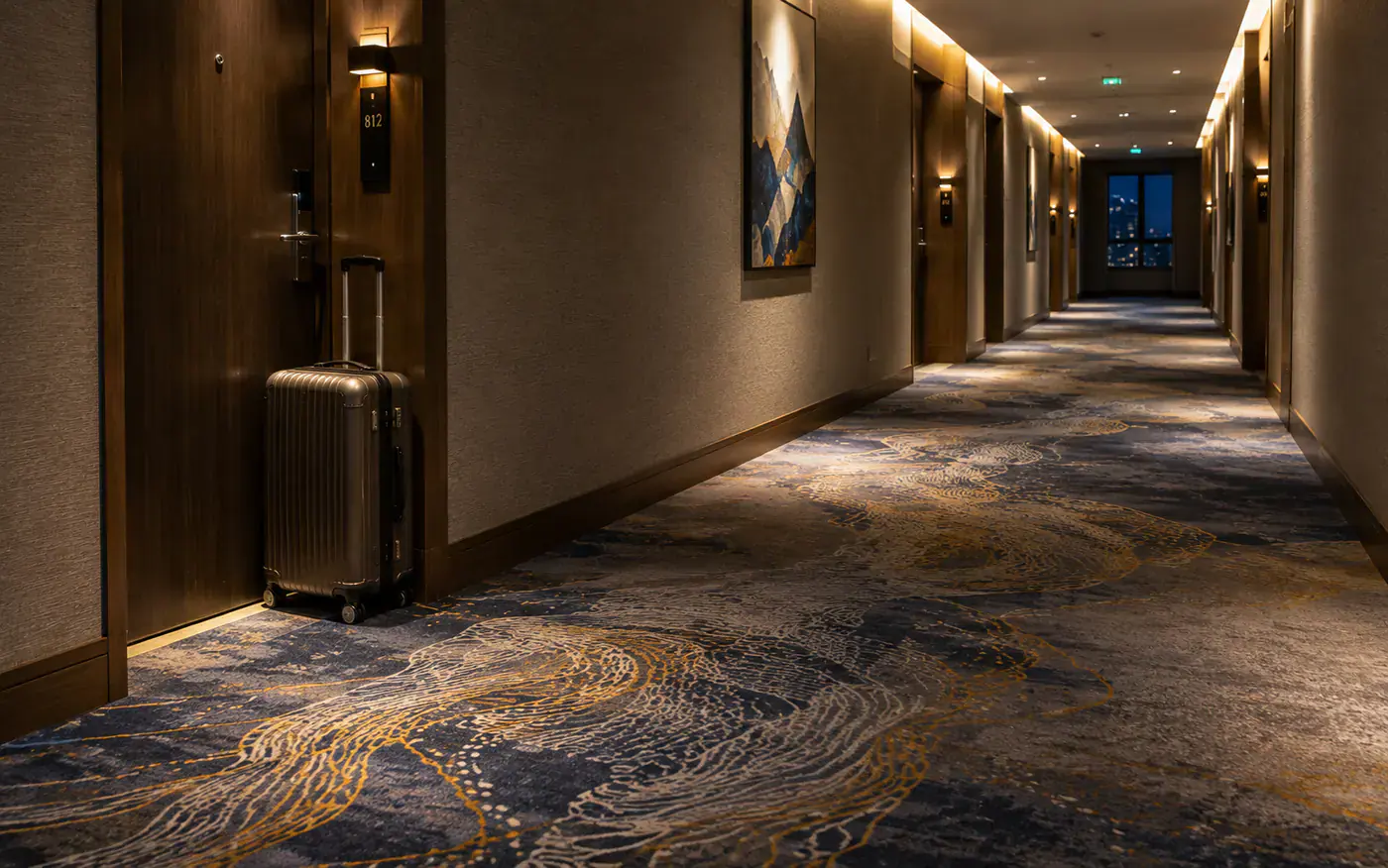 Luxury hotel corridor with patterned broadloom carpet and luggage near a guestroom door